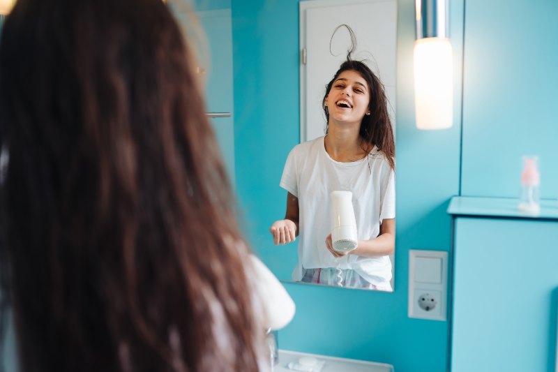 Portrait of young woman using hairdryer in bathroom. Having fun