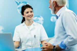 Young happy nurse on duty communicating with mature man at reception desk at clinic.