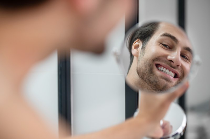 Appearance. Young man examining his face while watching into the round mirror