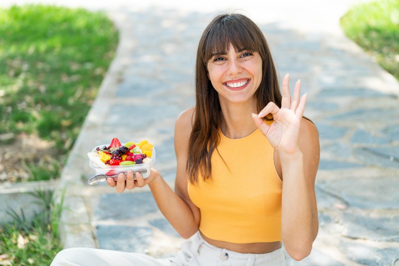 Young woman holding a bowl of fruit at outdoors showing ok sign with fingers